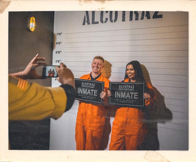 Couple taking mug shot photos during date night at Alcotraz - interactive element of this immersive prison bar experience.