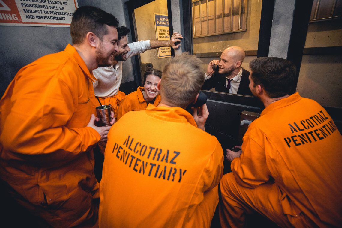 Inmates enjoying cocktails in prison cells at Alcotraz - immersive prison bar experience perfect for group activities.